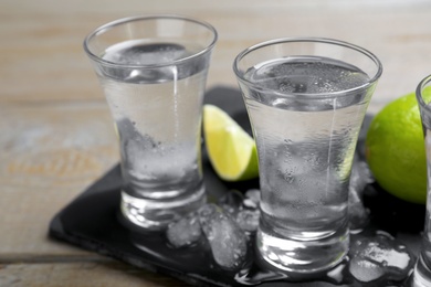 Photo of Shots of vodka, lime and ice on wooden table
