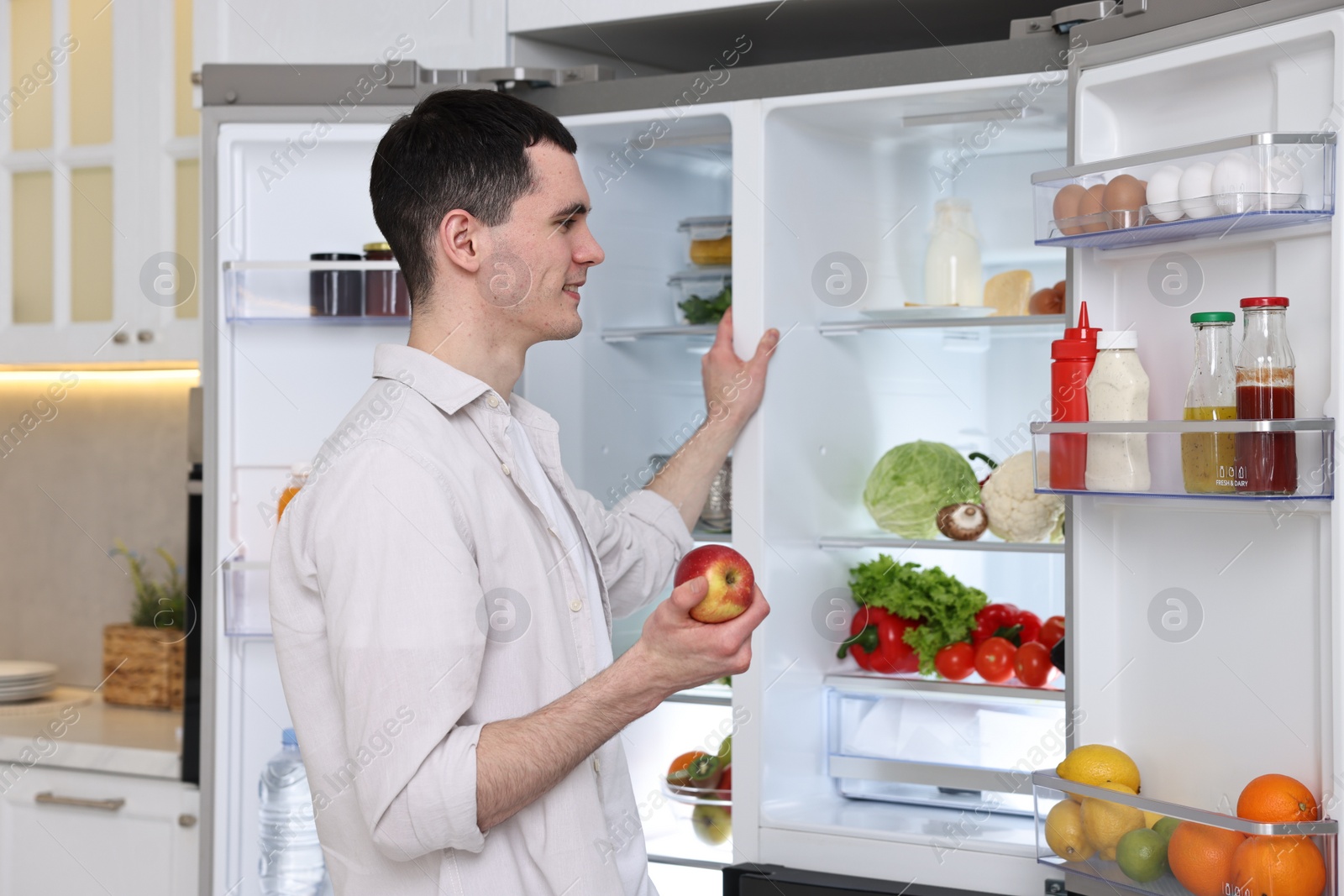 Photo of Happy man holding apple near refrigerator in kitchen