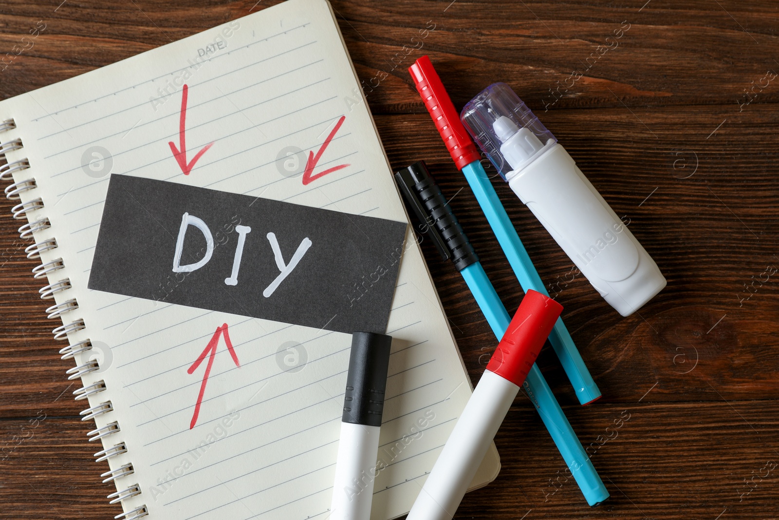 Photo of Notebook with abbreviation DIY, markers and correction pen on wooden table, flat lay