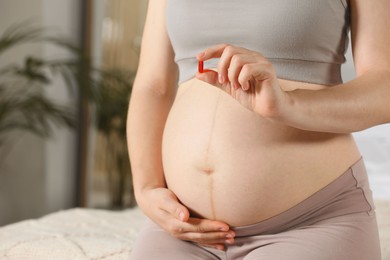 Pregnant woman taking pill indoors, closeup view