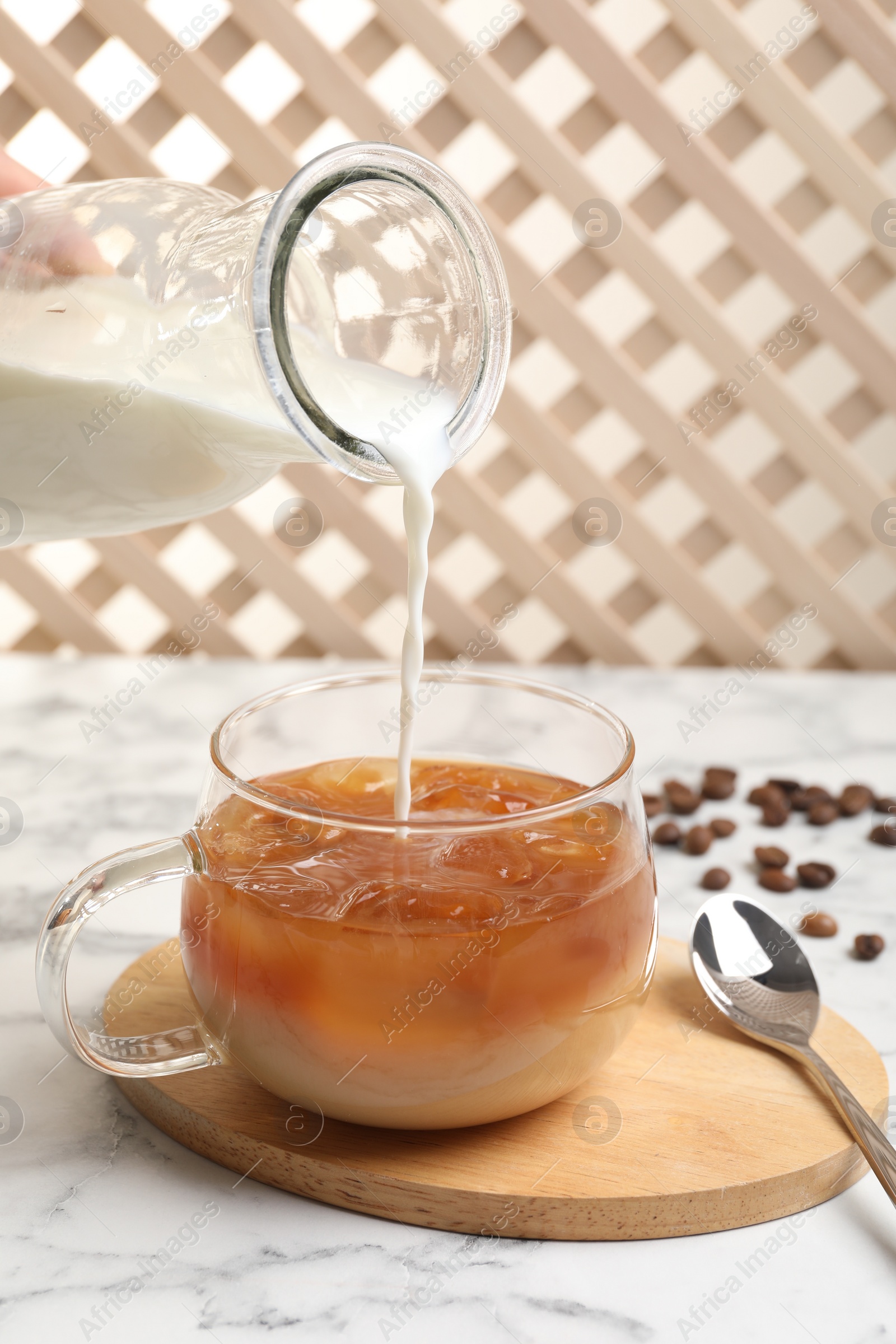 Photo of Woman pouring milk into glass with refreshing iced coffee at white marble table, closeup