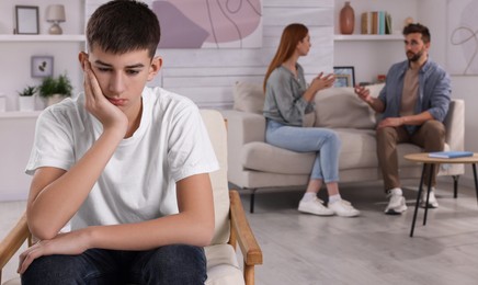 Photo of Unhappy teenage boy sitting in armchair while his parents arguing on background. Problems at home