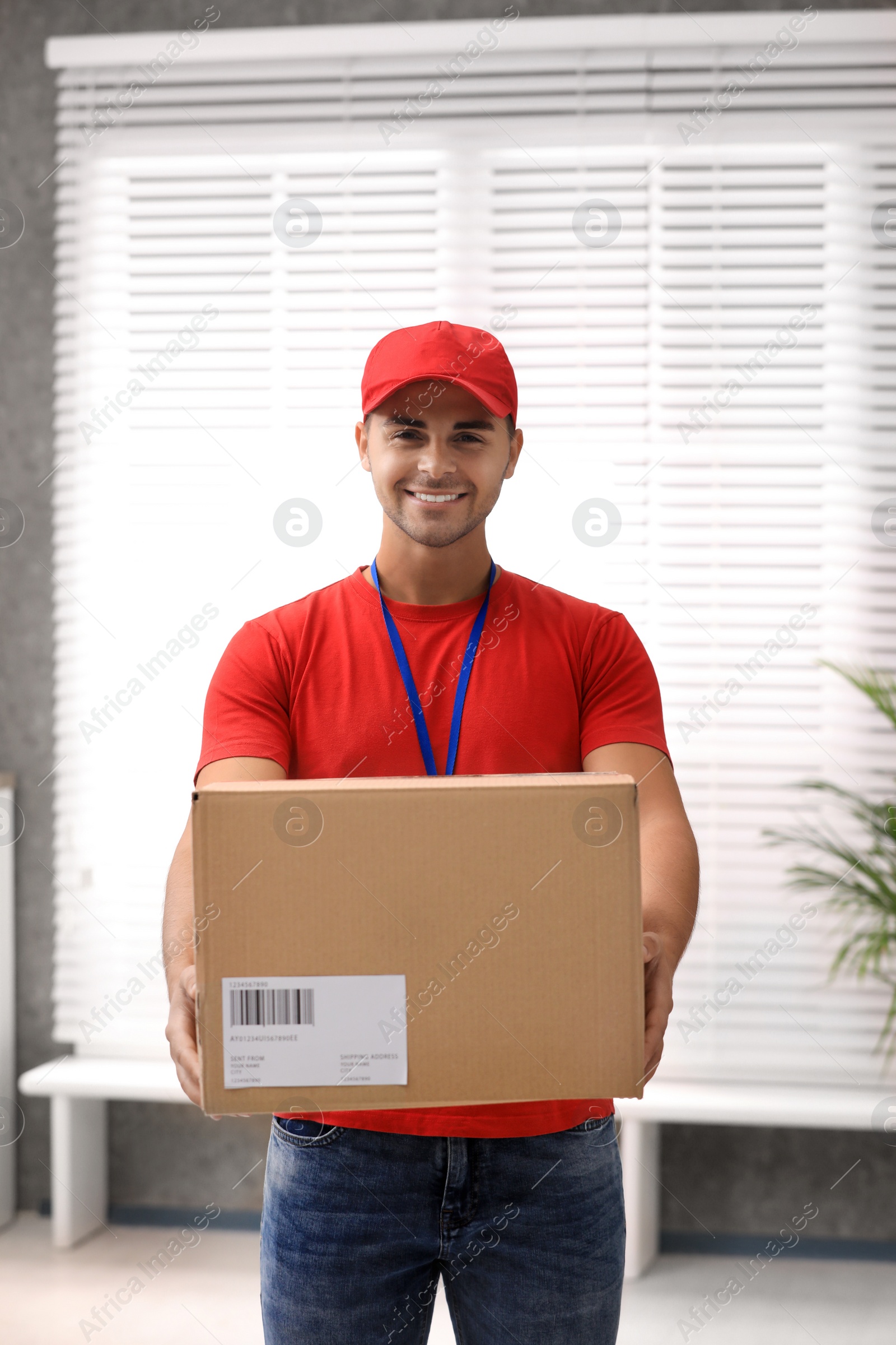 Photo of Young courier holding parcel indoors. Delivery service