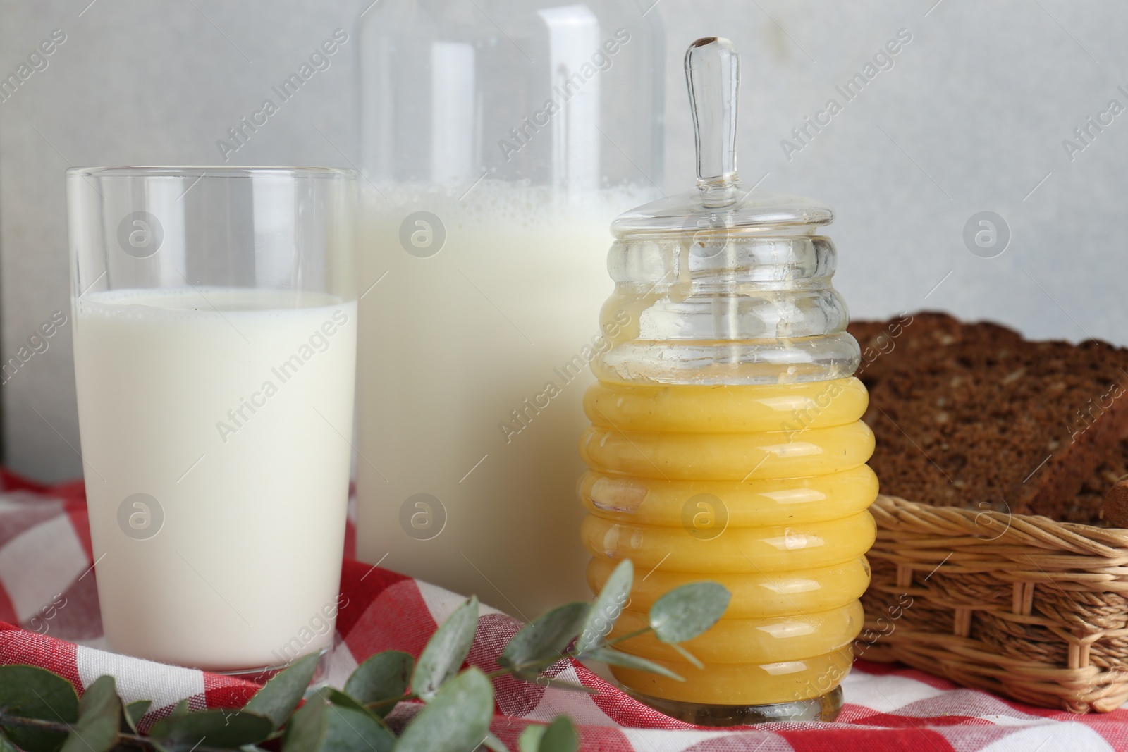 Photo of Jar with tasty honey, milk and bread on checkered cloth