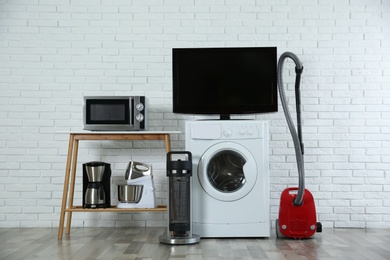 Photo of Modern vacuum cleaner and different household appliances near white brick wall indoors