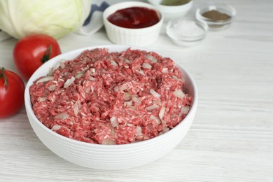 Photo of Meat filling in bowl and other ingredients for stuffed cabbage rolls on white wooden table