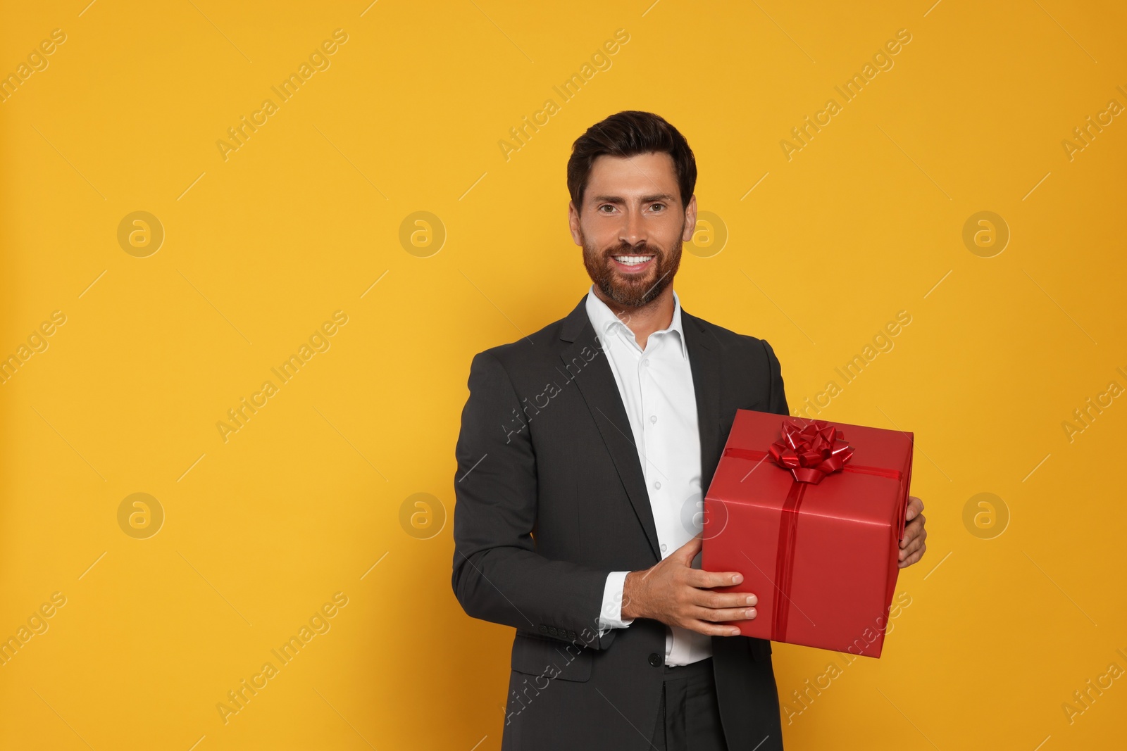 Photo of Handsome man holding gift box on yellow background, space for text