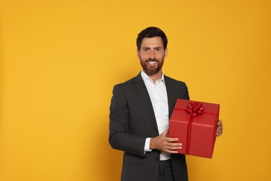 Handsome man holding gift box on yellow background, space for text