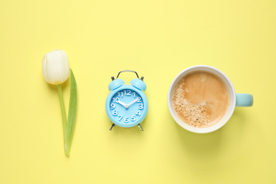 Photo of White tulip, alarm clock and coffee on yellow background, flat lay