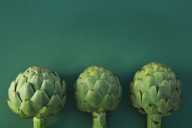 Photo of Whole fresh raw artichokes on green background, flat lay. Space for text