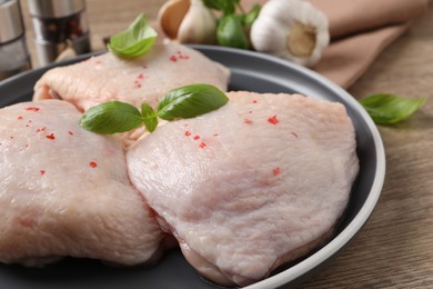 Photo of Raw chicken thighs with basil on wooden table, closeup