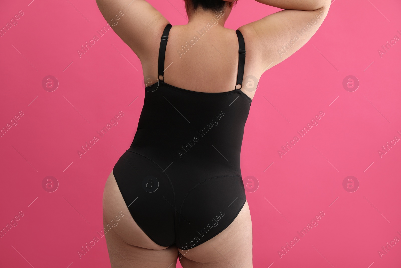 Photo of Back view of overweight woman in black underwear on pink background, closeup. Plus-size model