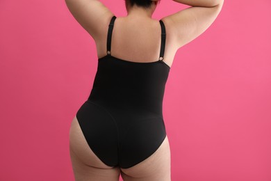 Back view of overweight woman in black underwear on pink background, closeup. Plus-size model