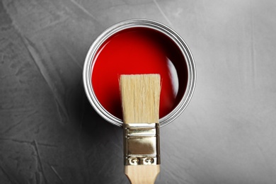 Photo of Can with red paint and brush on gray background, top view