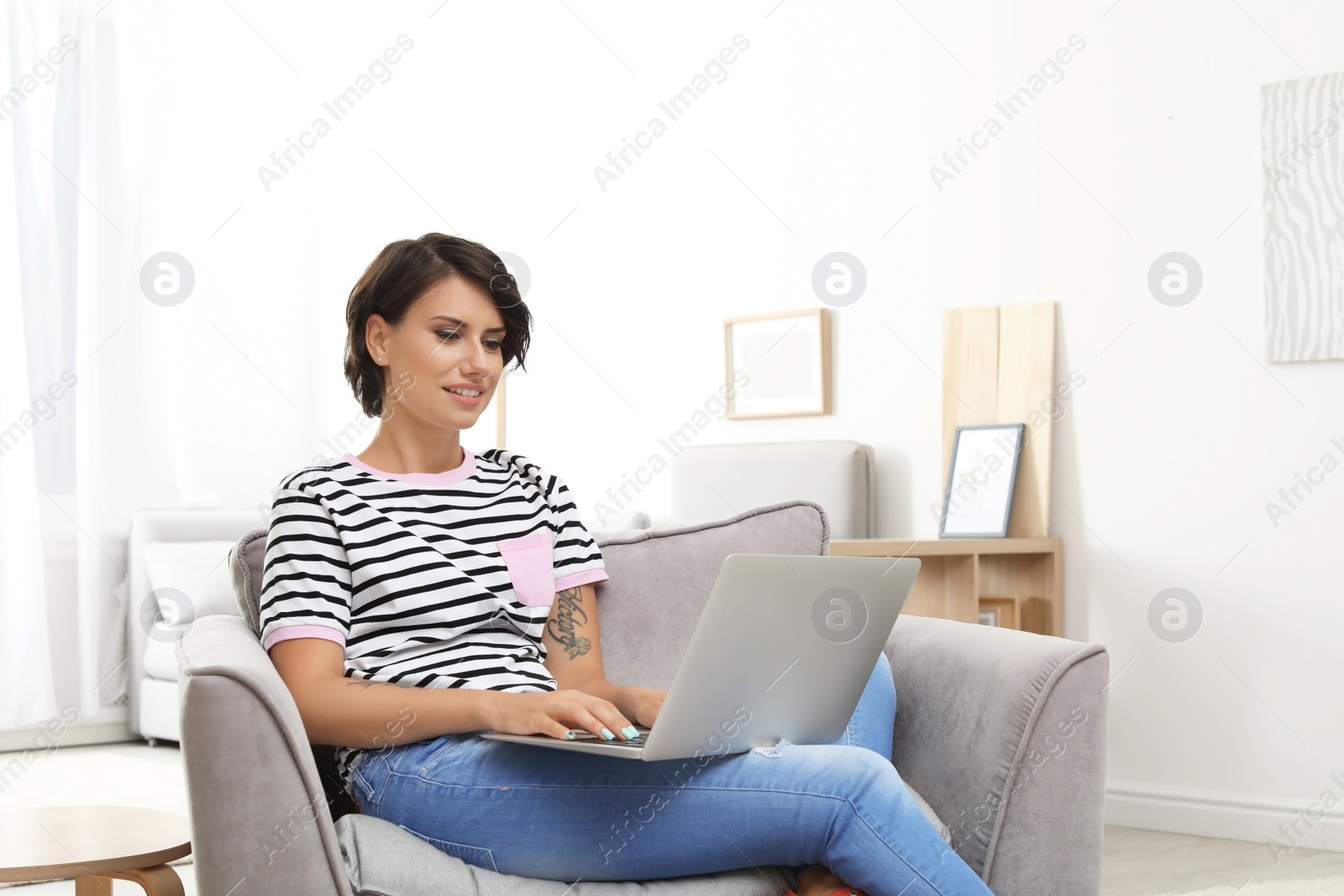 Photo of Young woman with modern laptop sitting in armchair at home