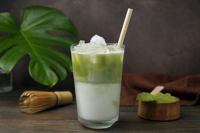 Photo of Glass of tasty iced matcha latte, bamboo whisk and powder on wooden table