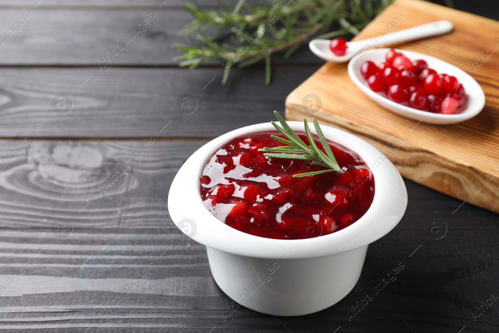 Photo of Fresh cranberry sauce in bowl and rosemary on black wooden table, closeup. Space for text