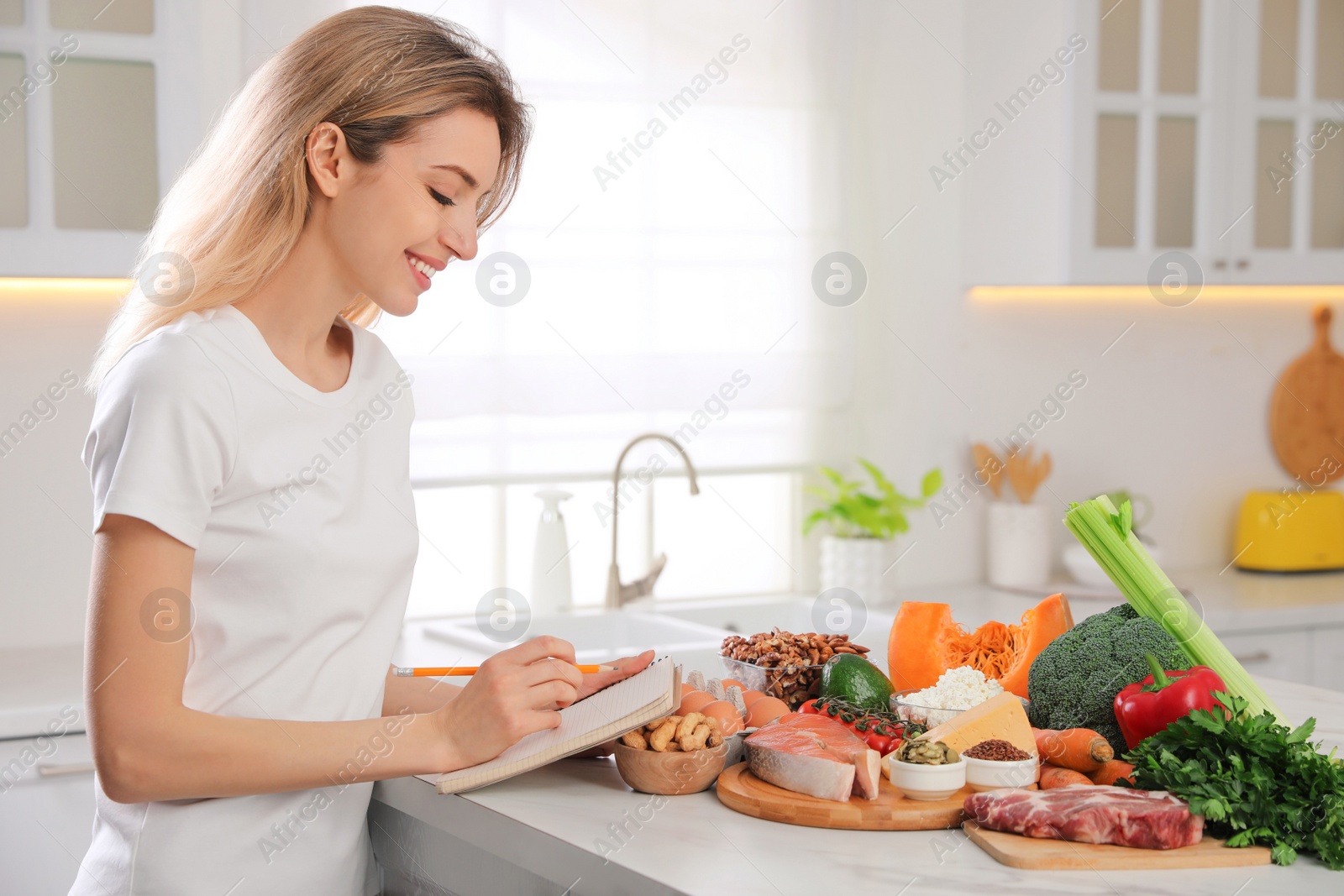 Photo of Woman with notebook and healthy food at white table in kitchen. Keto diet