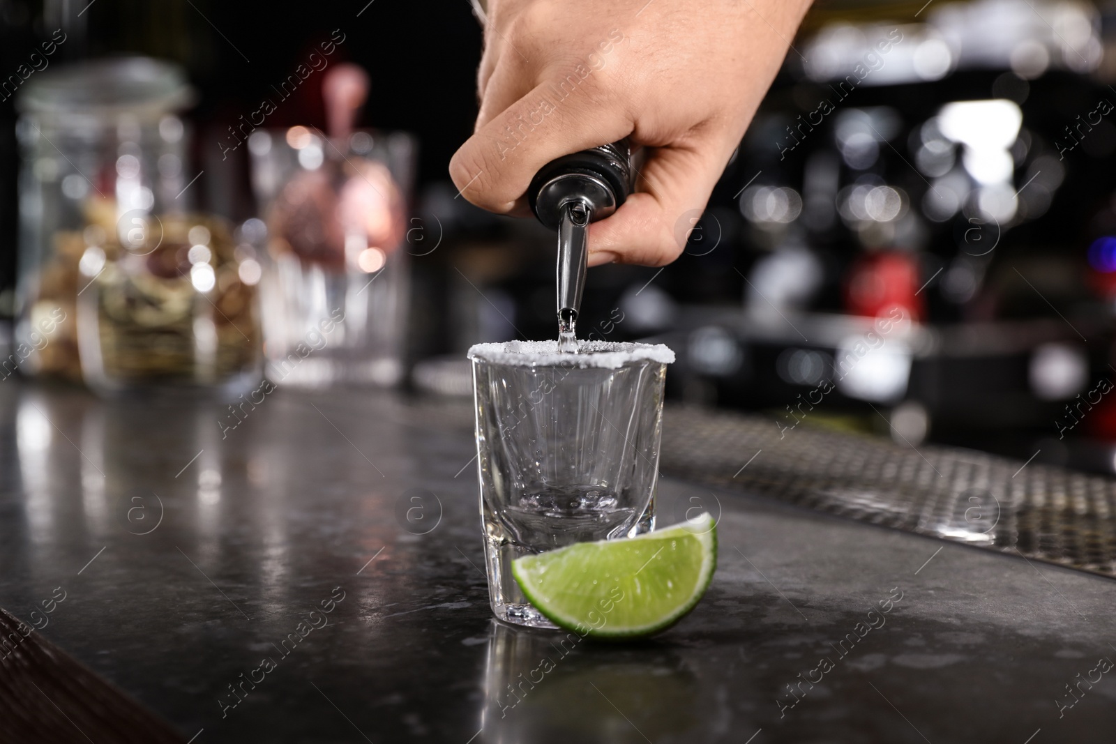 Photo of Bartender pouring Mexican Tequila into shot glass at bar counter, closeup