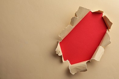 Photo of Hole in light beige paper on red background, space for text