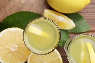 Tasty limoncello liqueur, lemons and green leaves on table, flat lay