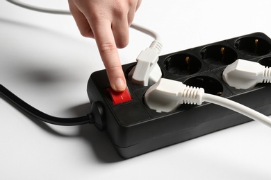 Photo of Woman pressing power button of extension cord on white background, closeup. Electrician's equipment