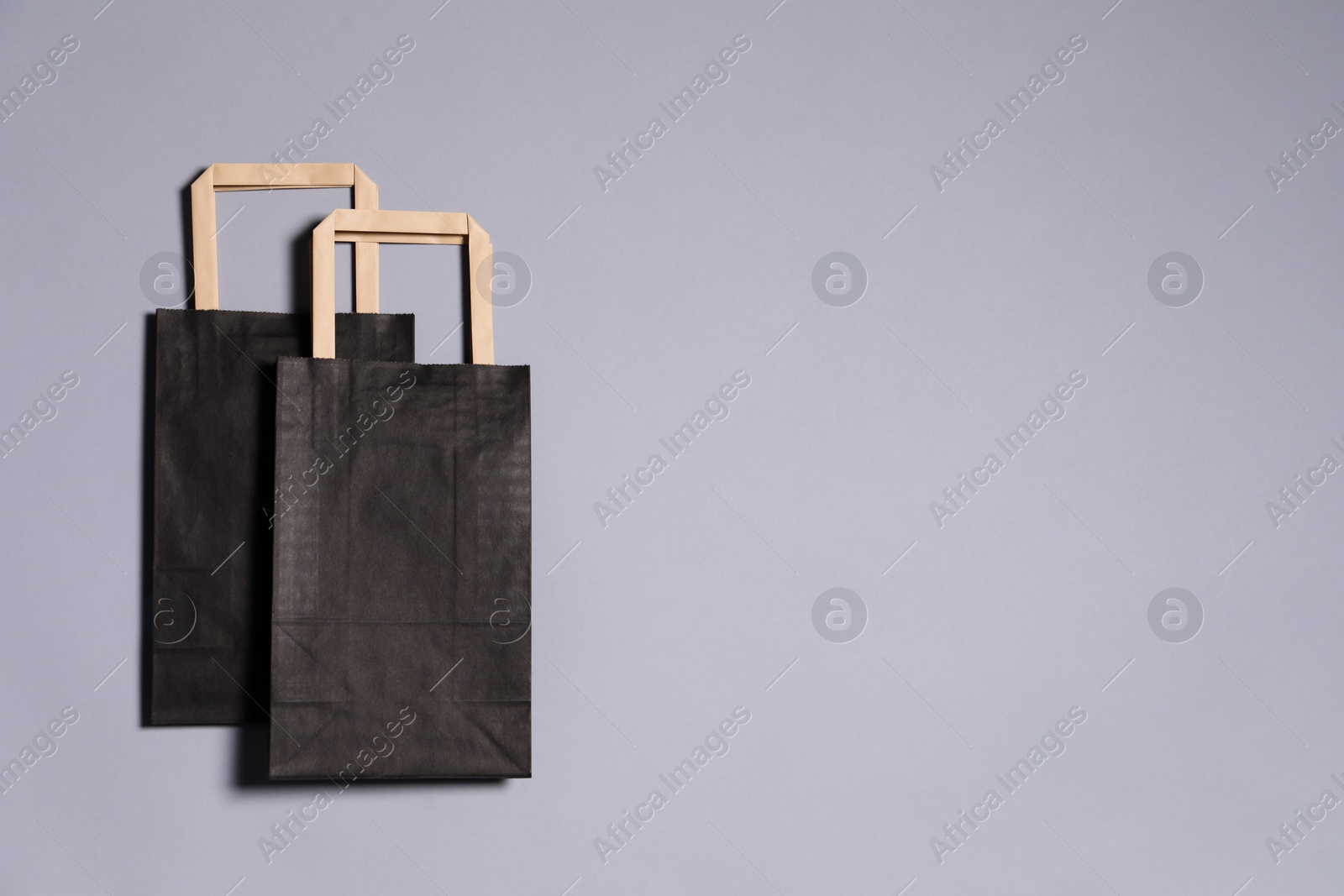 Photo of Two black paper shopping bags on grey background, top view. Space for text