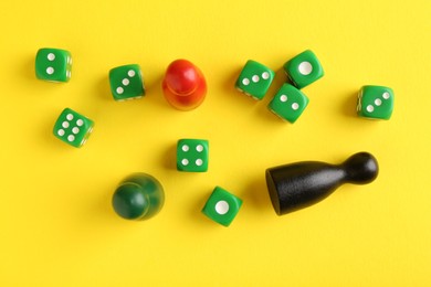 Many green dices and color game pieces on yellow background, flat lay