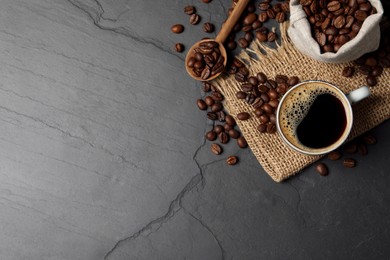 Photo of Cup of aromatic coffee and beans on black table, flat lay. Space for text