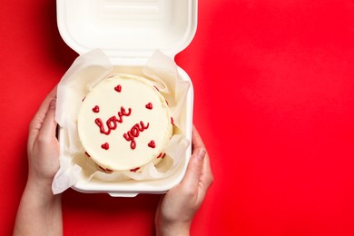 Photo of Woman holding takeaway box with bento cake at red table, top view. St. Valentine's day surprise