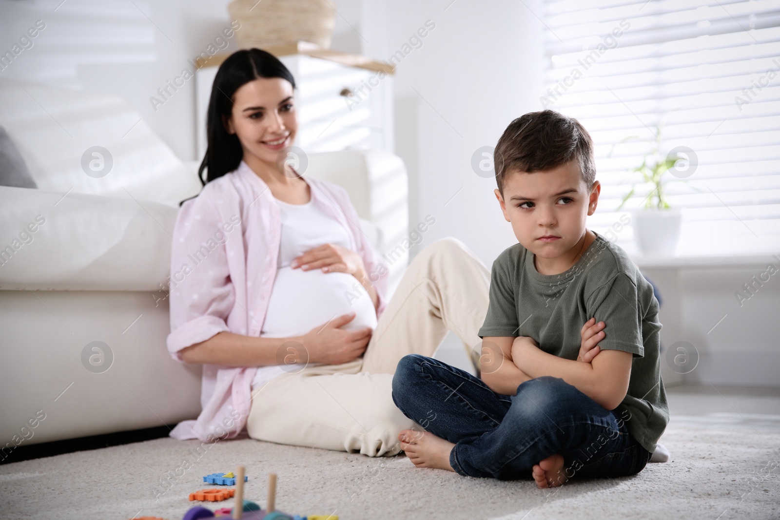 Photo of Unhappy little boy near pregnant mother at home. Feeling jealous towards unborn sibling