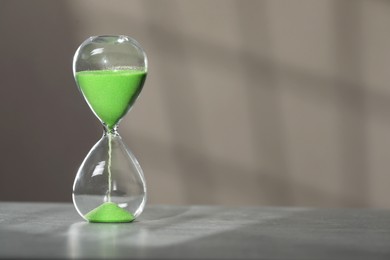 Photo of Hourglass with green flowing sand on table against light grey background, space for text
