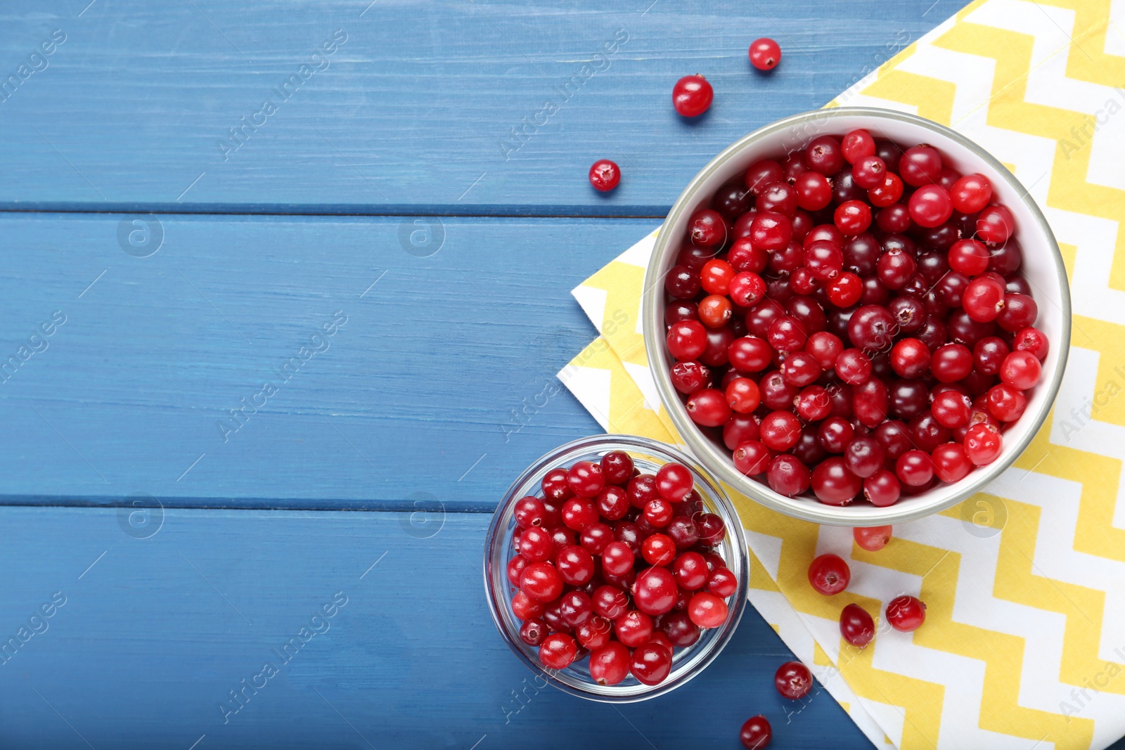 Photo of Fresh ripe cranberries in bowls on blue wooden table, top view. Space for text