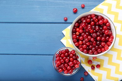 Fresh ripe cranberries in bowls on blue wooden table, top view. Space for text