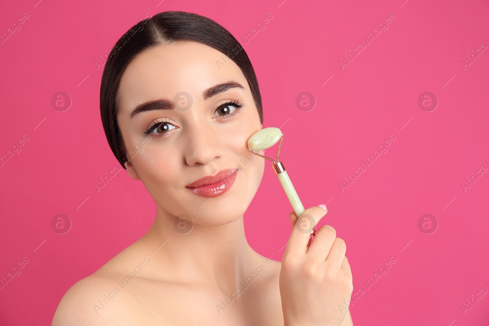 Photo of Woman using natural jade face roller on pink background, space for text