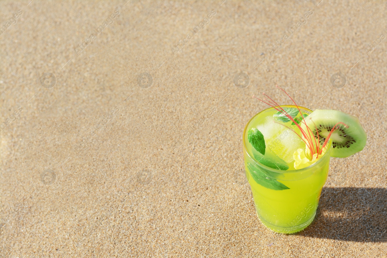 Glass of refreshing drink with kiwi and mint on sand. Space for text Photo of Glass of refreshing drink with kiwi and mint on sand. Space for text