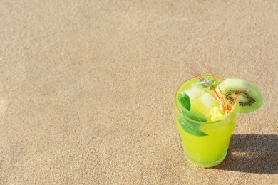 Photo of Glass of refreshing drink with kiwi and mint on sand. Space for text