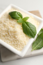 Photo of Square bowl with grated parmesan cheese and basil on white table, above view