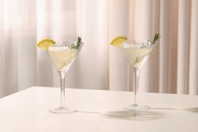 Photo of Elegant martini glasses with fresh cocktail, rosemary and lemon slices on white table indoors