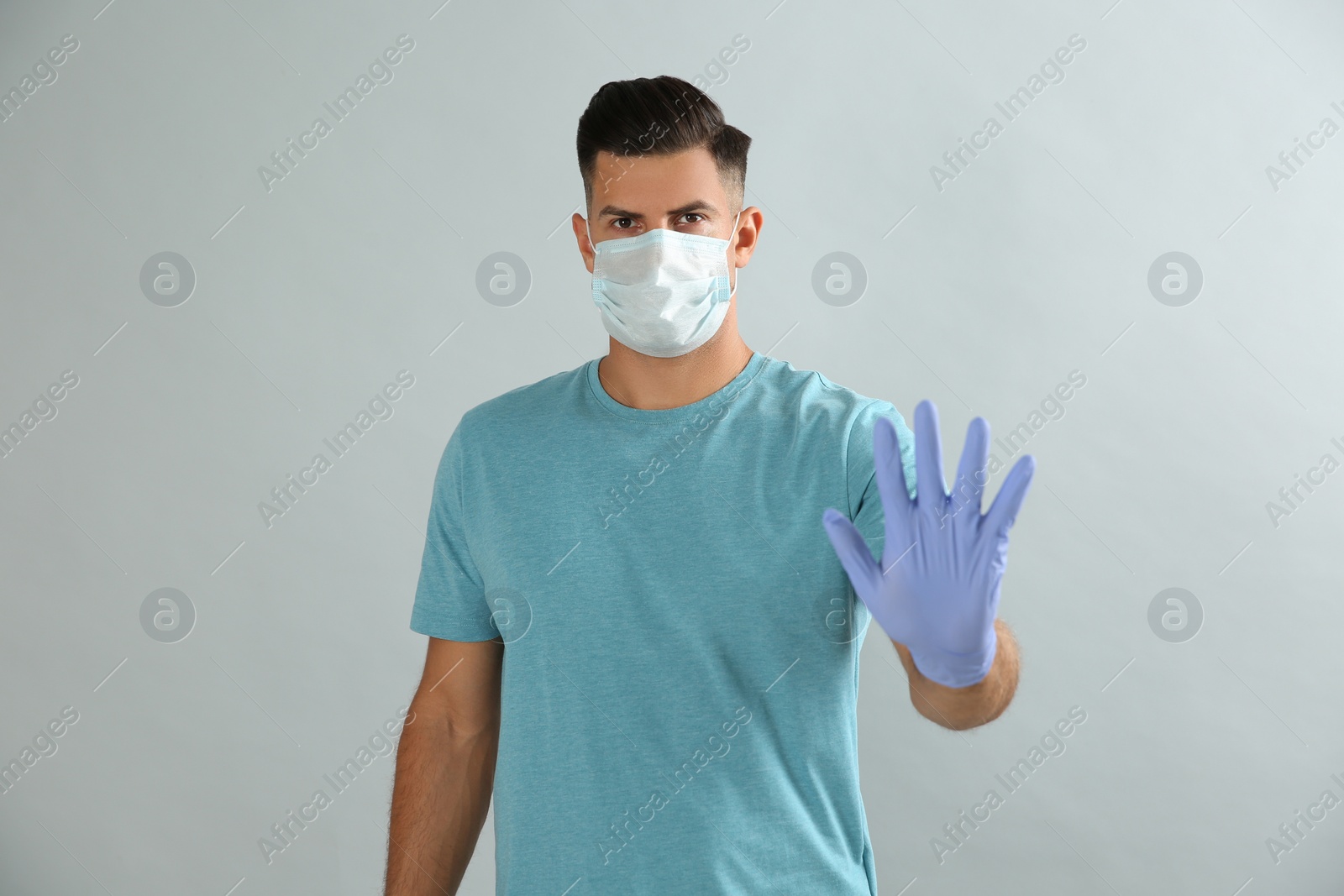 Photo of Man in protective face mask and medical gloves showing stop gesture on grey background
