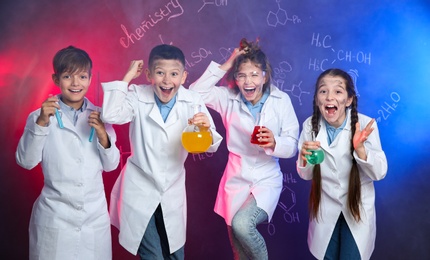 Photo of Emotional pupils holding flasks against blackboard with chemistry formulas