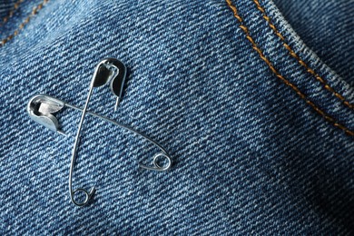 Photo of Metal safety pins on denim fabric, closeup