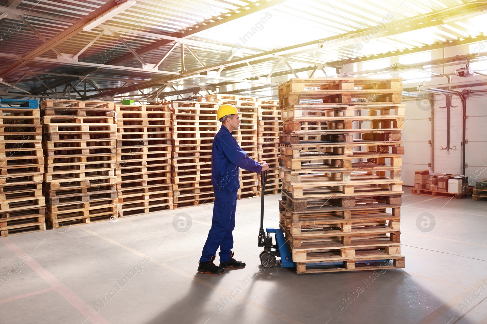 Image of Worker moving wooden pallets with manual forklift in warehouse