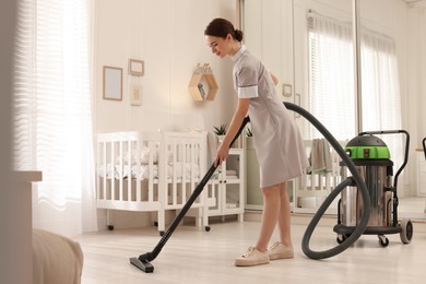 Photo of Professional chambermaid vacuuming floor in nursery. Cleaning service