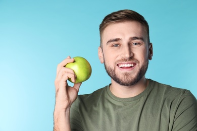 Photo of Young man with healthy teeth and apple on color background. Space for text