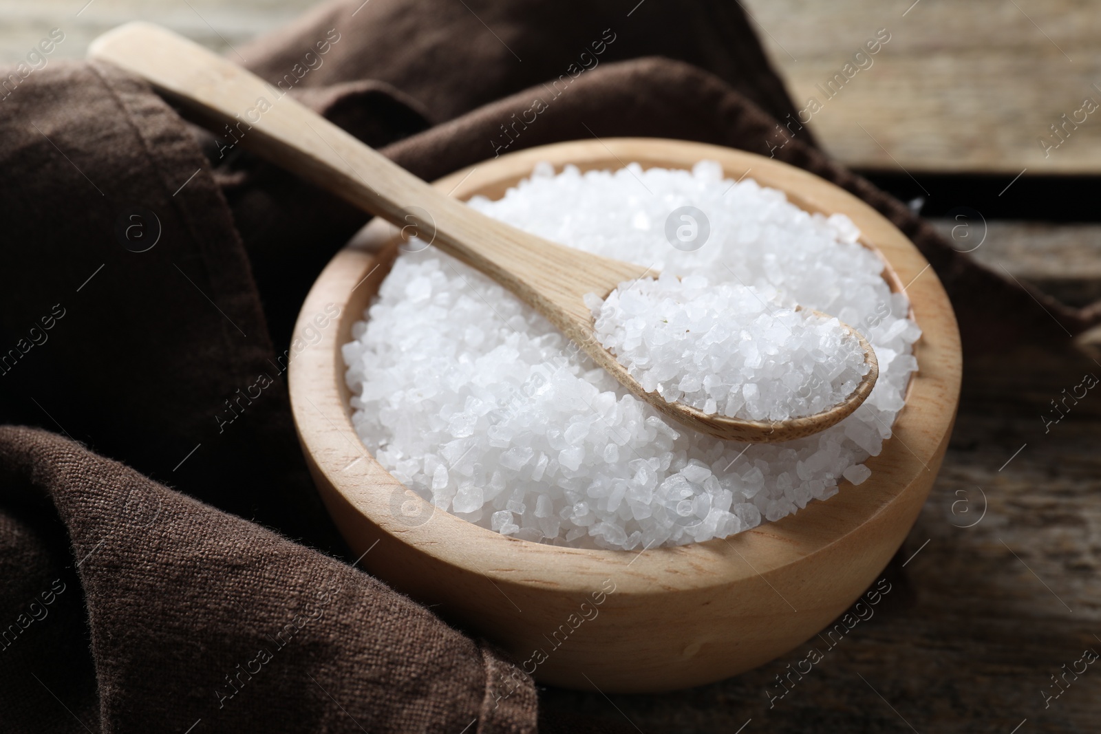 Photo of Organic salt in bowl and spoon on wooden table, closeup