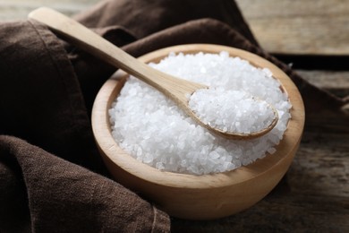 Photo of Organic salt in bowl and spoon on wooden table, closeup