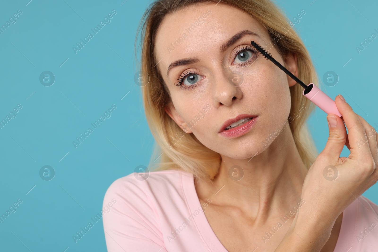 Photo of Beautiful woman applying mascara on light blue background, closeup. Space for text