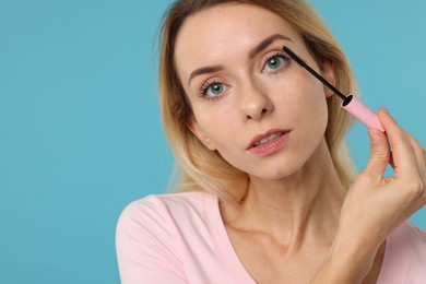 Beautiful woman applying mascara on light blue background, closeup. Space for text