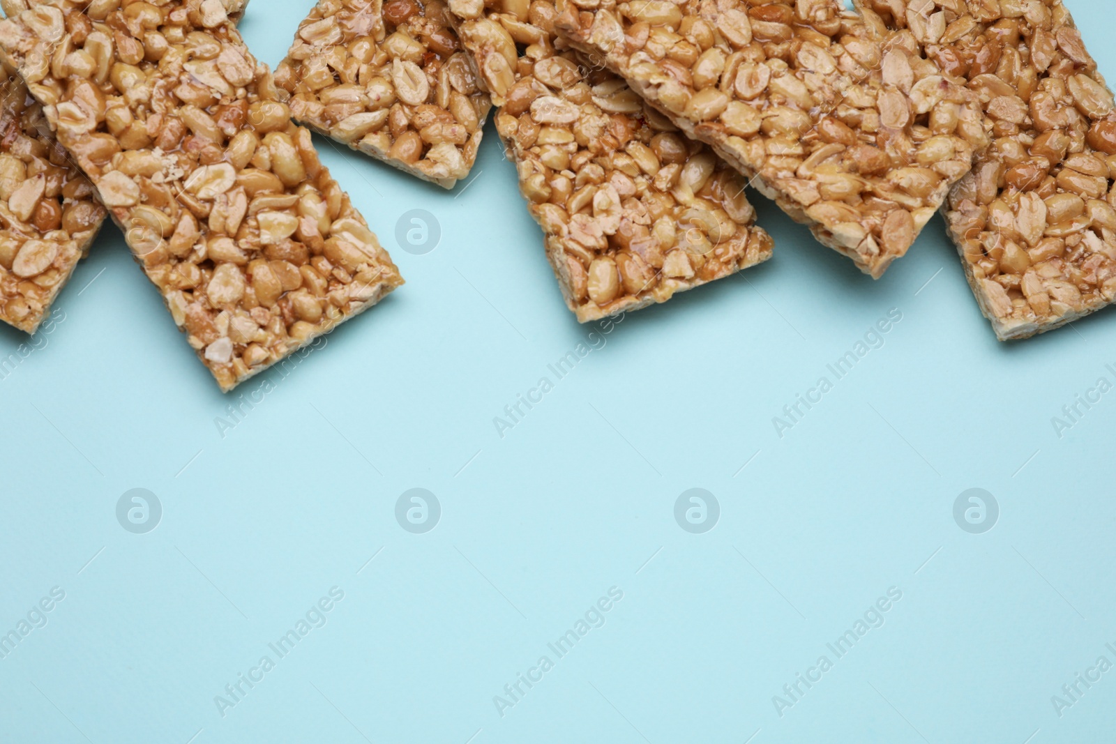 Photo of Tasty peanut bars (kozinaki) on light blue background, flat lay. Space for text